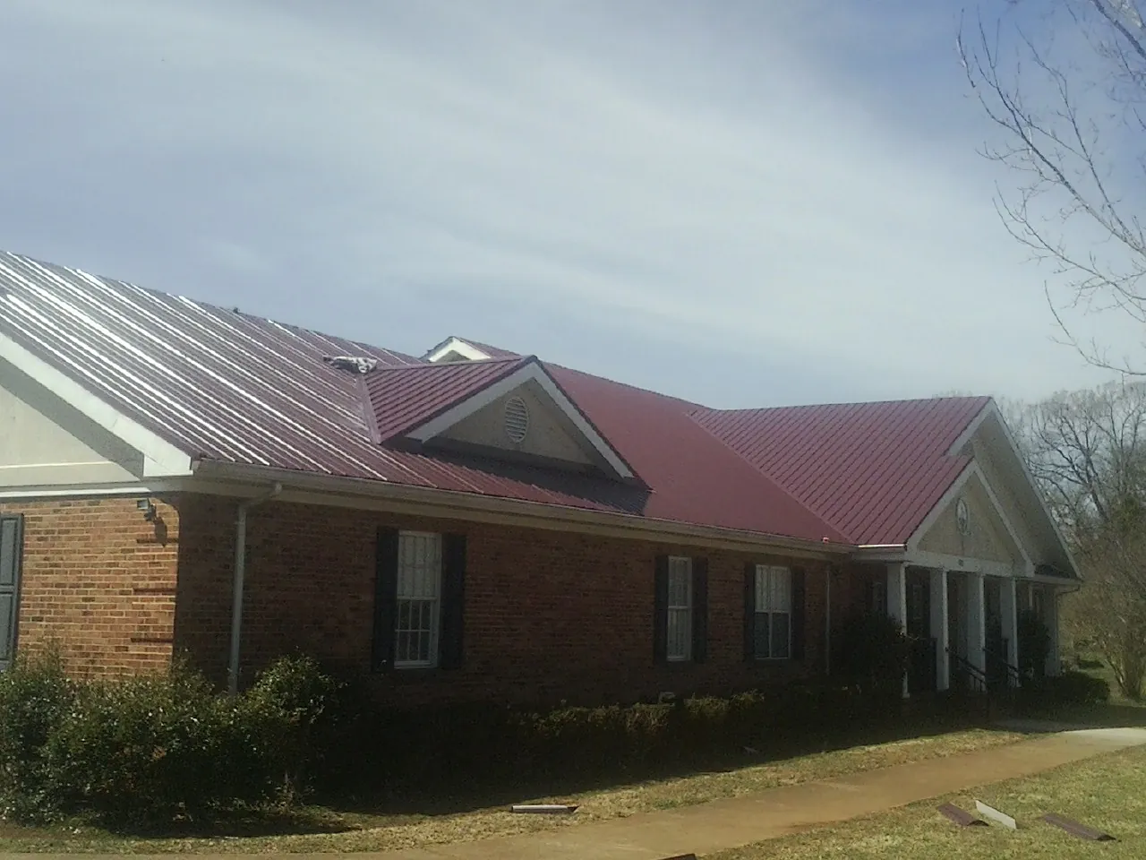 Red metal roof with gabled entries on a long brick building, from a Hail Damage Roof Repair job in Fort Gaines