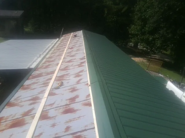Old rusted panels beside newly installed green metal roofing — Wind Damage Roof Repair by Roofing Brothers in Fort Gaines