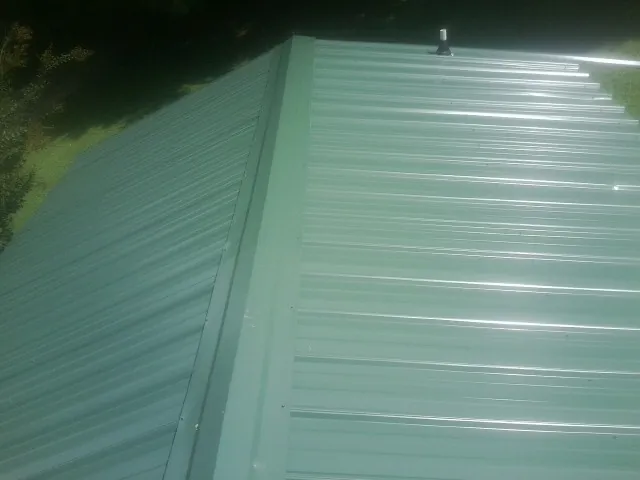 New green metal panels meeting at the ridge of a roof — Flat Roof Repair work by our crew in Fort Gaines