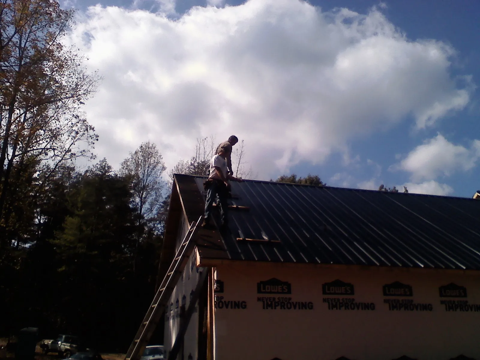 Roofer fastening dark metal panels high against a cloudy sky, from a Roof Inspection job in Fort Gaines