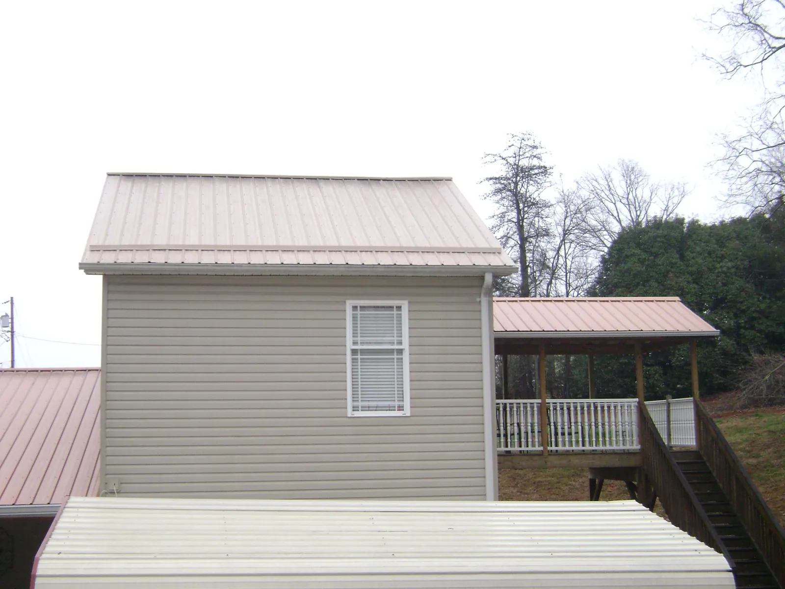 Tan metal roofs on a two story addition and attached porch, from a Roof Replacement job in Fort Gaines